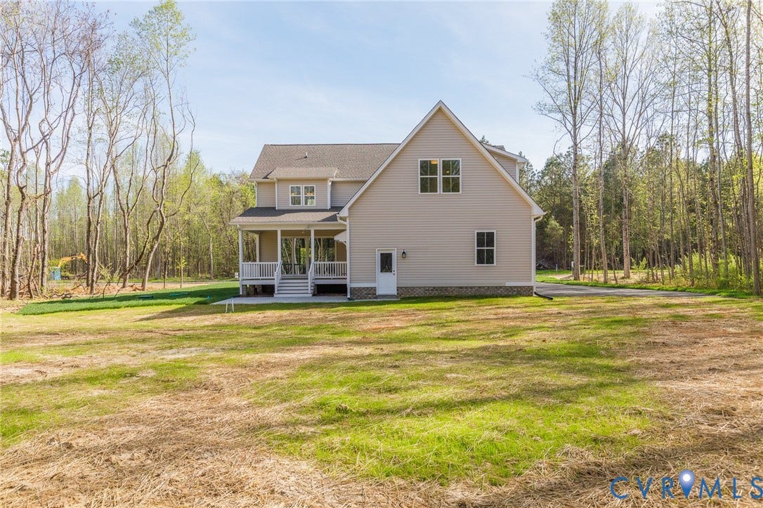 The property features a spacious yard with a mix of green grass and natural areas, bordered by a dense woodland