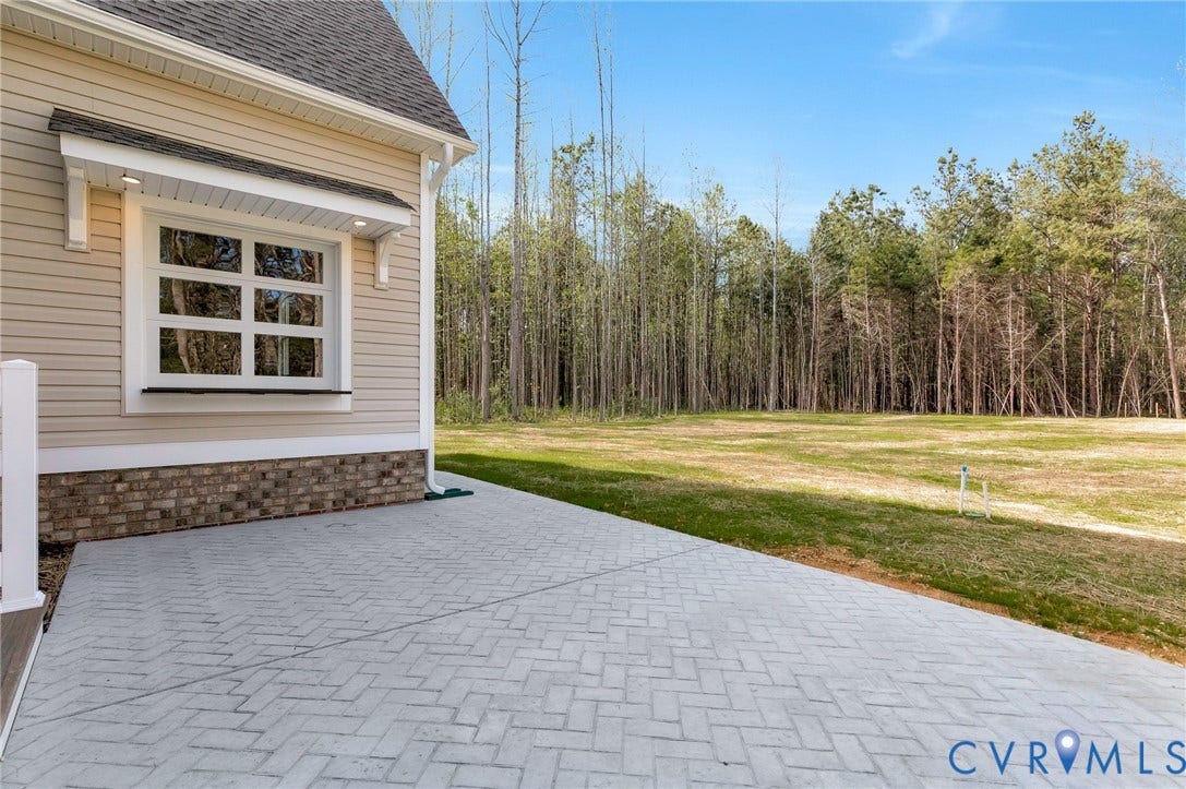 The property features a spacious paved patio area, bordered by a well-maintained lawn and a backdrop of mature trees