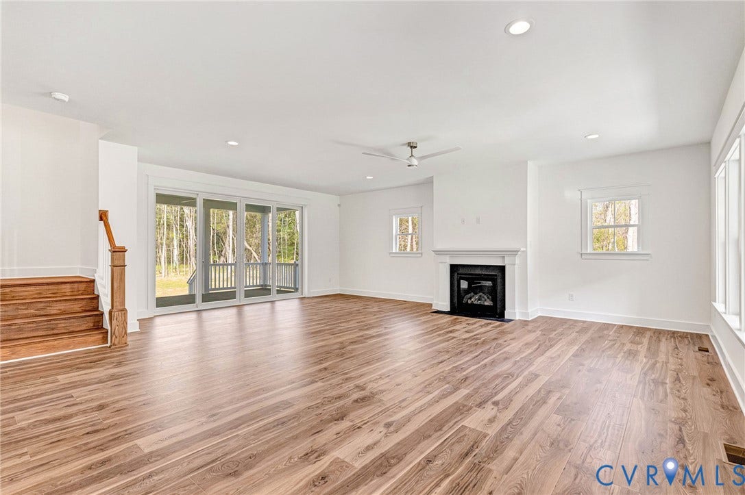 Spacious living area featuring light wood flooring, a fireplace with a white mantel, and large sliding glass doors leading to a porch
