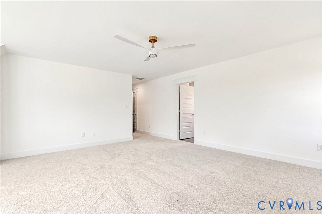 Spacious interior room with light-colored carpeting, white walls, and a contemporary ceiling fan with a gold-toned fixture