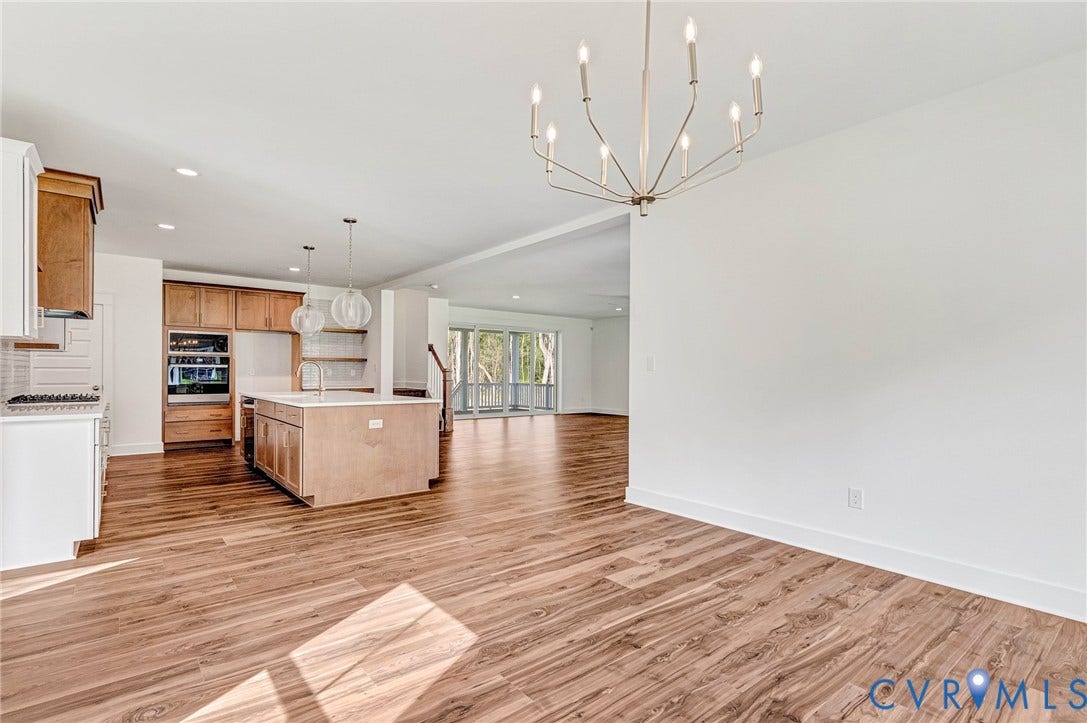 Spacious open-concept living area featuring hardwood flooring, white walls, and a modern chandelier
