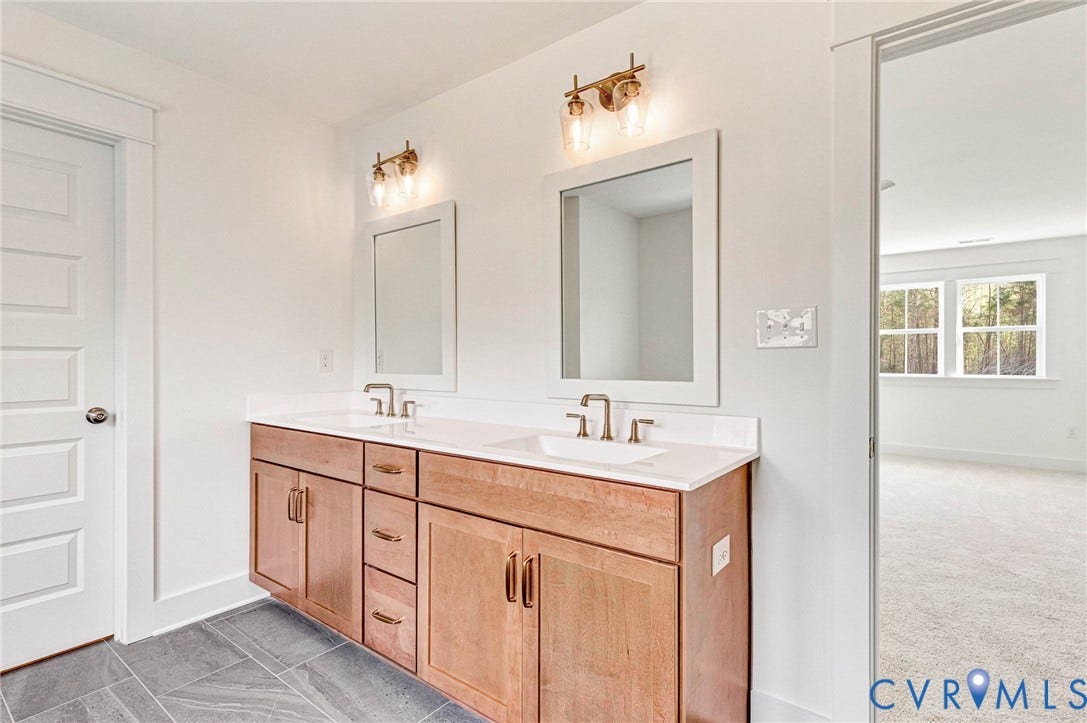 Bathroom featuring a dual vanity with light wood cabinetry, white countertops, and contemporary lighting fixtures