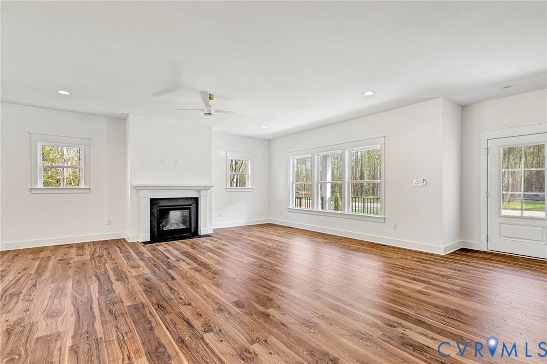 The living area features hardwood floors, a fireplace with a white mantel, and ample natural light from multiple windows and a glass-paneled door