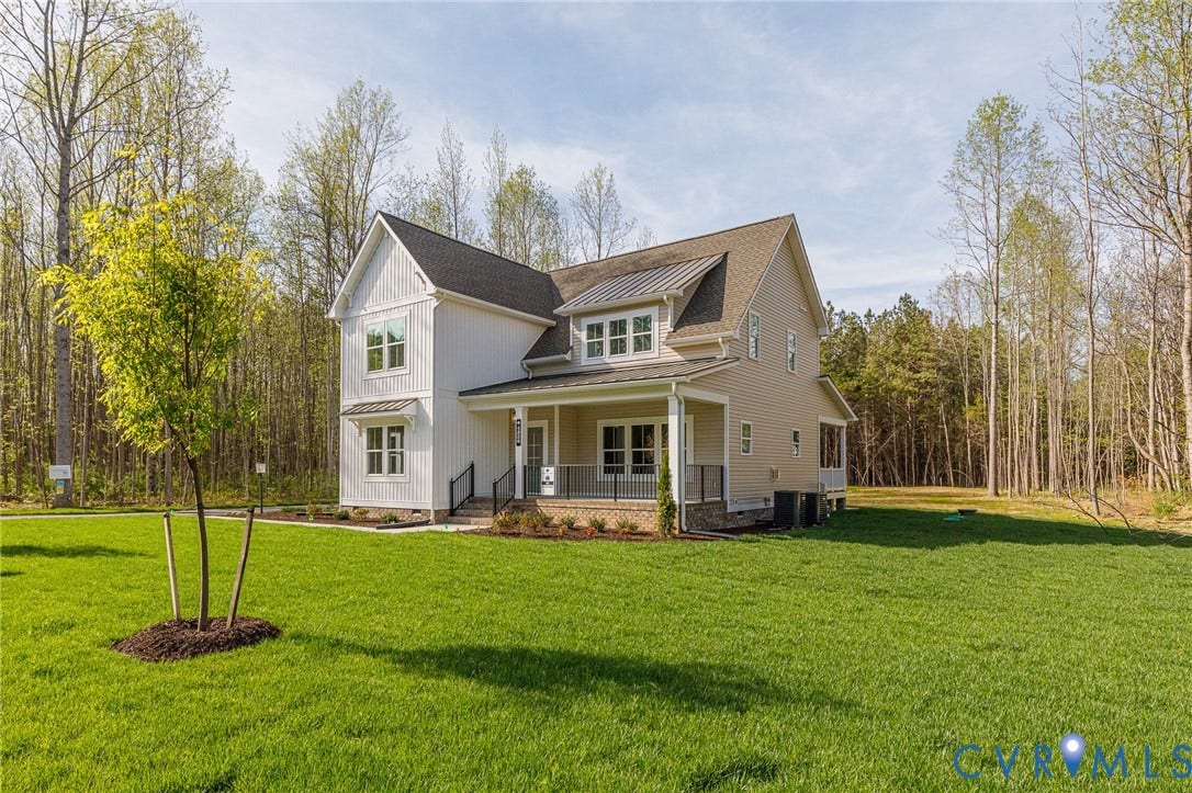 The property features a two-story residence with a covered front porch, a well-maintained lawn, and a backdrop of mature trees