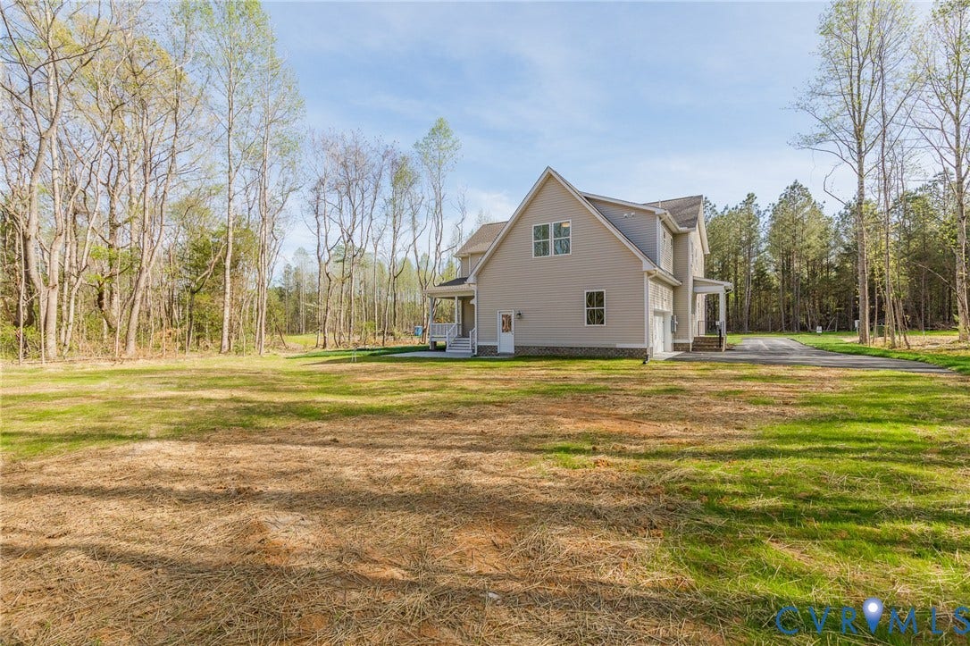 The property features a large yard with a mix of green grass and dry patches, surrounded by numerous mature trees