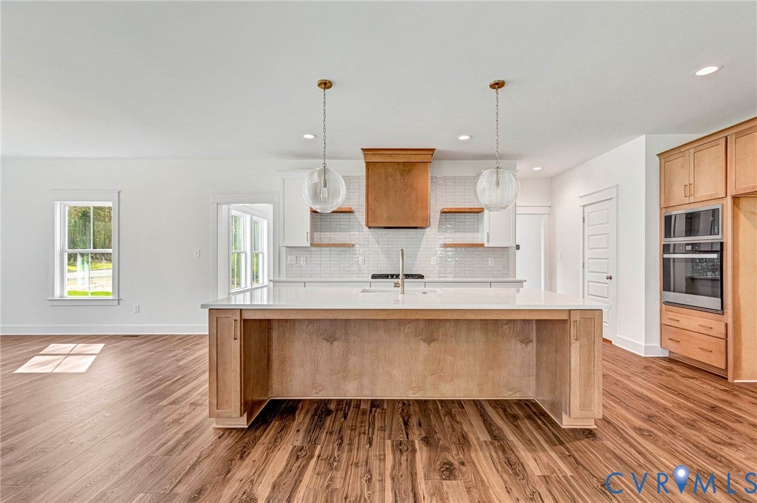 The kitchen features a large island with a light wood finish, white countertops, and two pendant lights