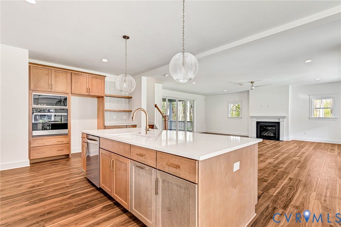 The property features a kitchen with a large island with a sink, light wood cabinetry, and a built-in oven and microwave