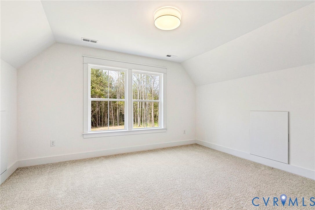 The room features a neutral carpet, white walls, and a window providing a view of trees