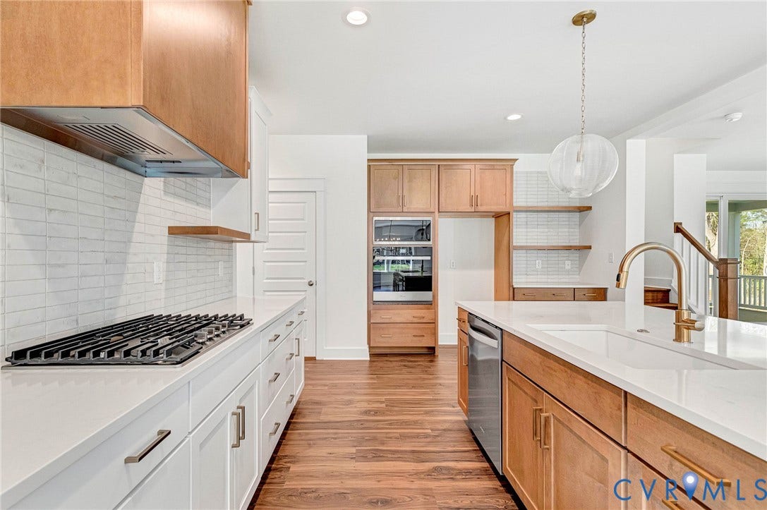 The kitchen features a gas range, white tile backsplash, and an island with a sink and gold-toned faucet
