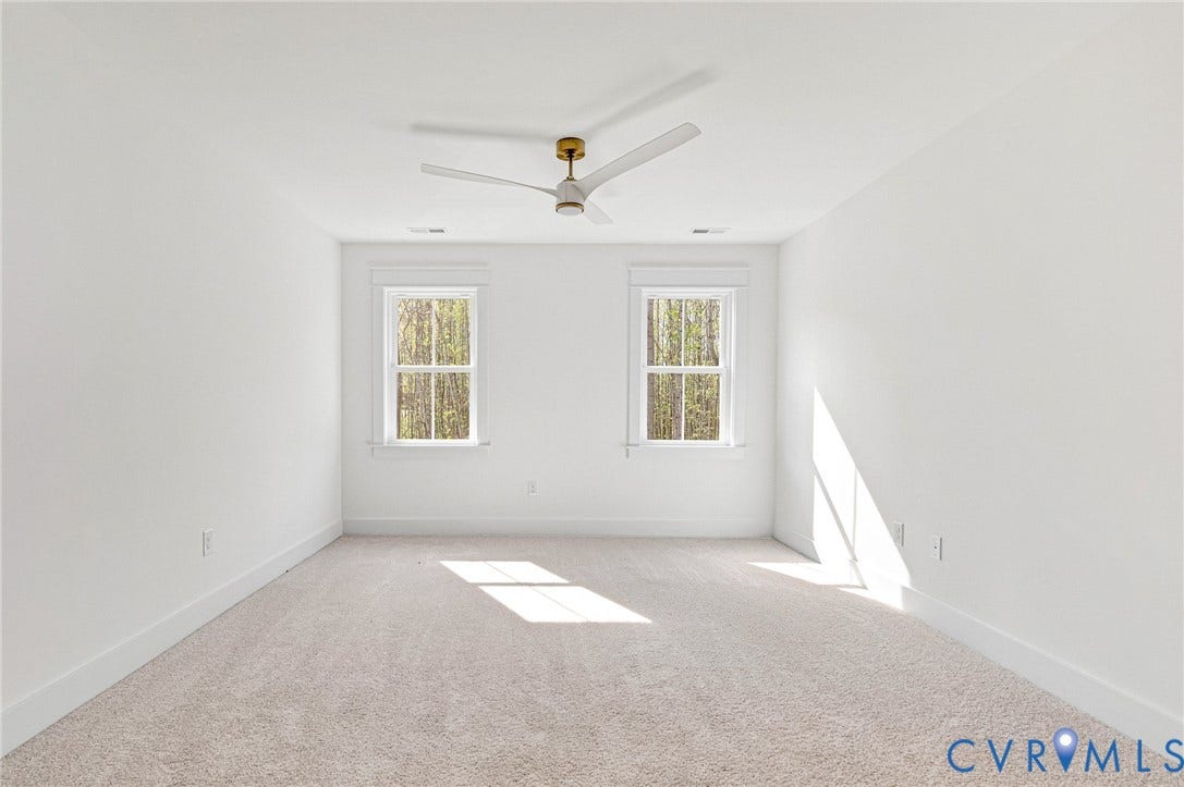 This room features light-colored carpeting, two windows, and a ceiling fan with a gold-toned fixture