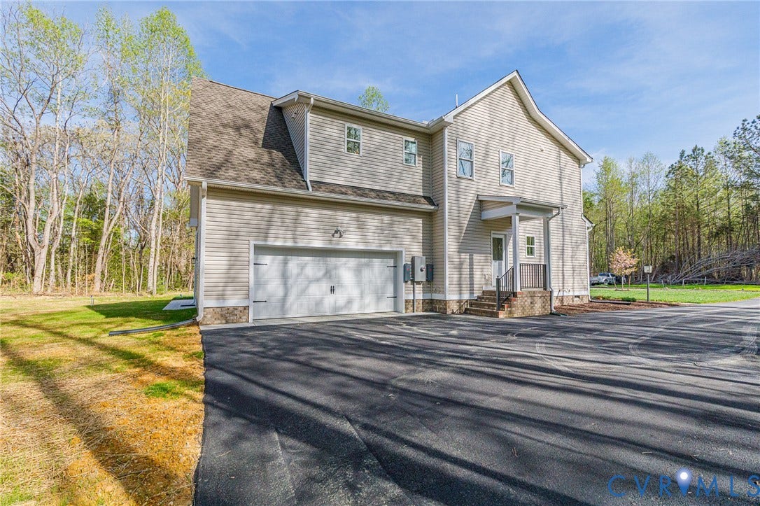 The property features a two-car garage with a paved driveway, and light-colored siding