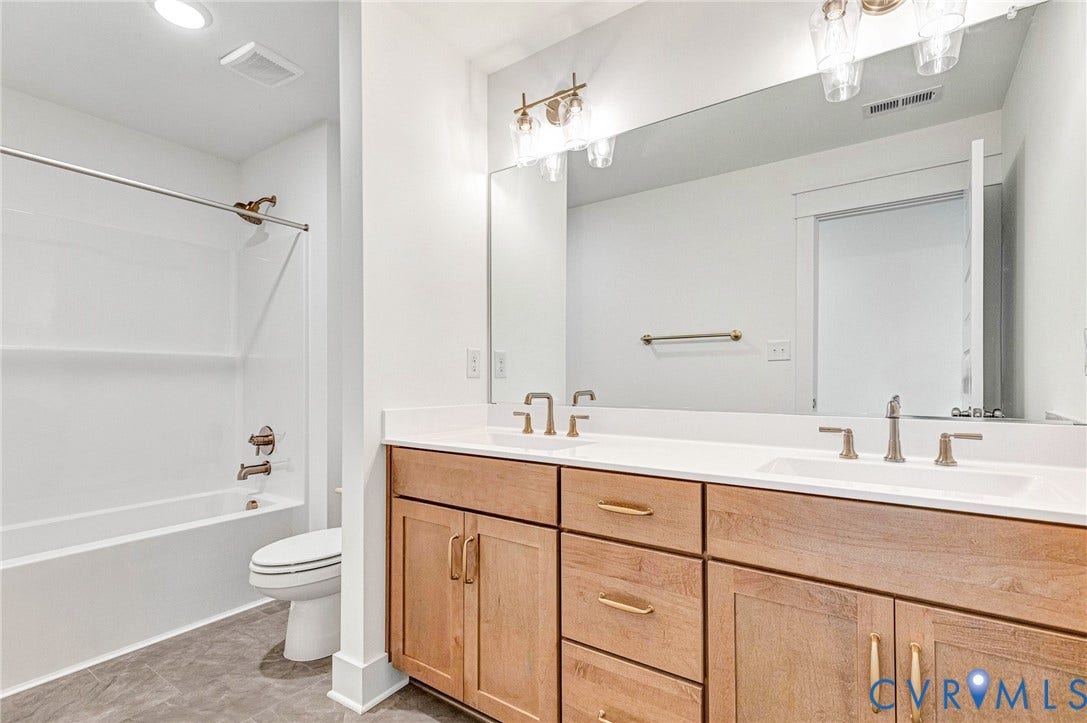 This bathroom features a double vanity with light wood cabinetry, a white countertop, and two vessel sinks