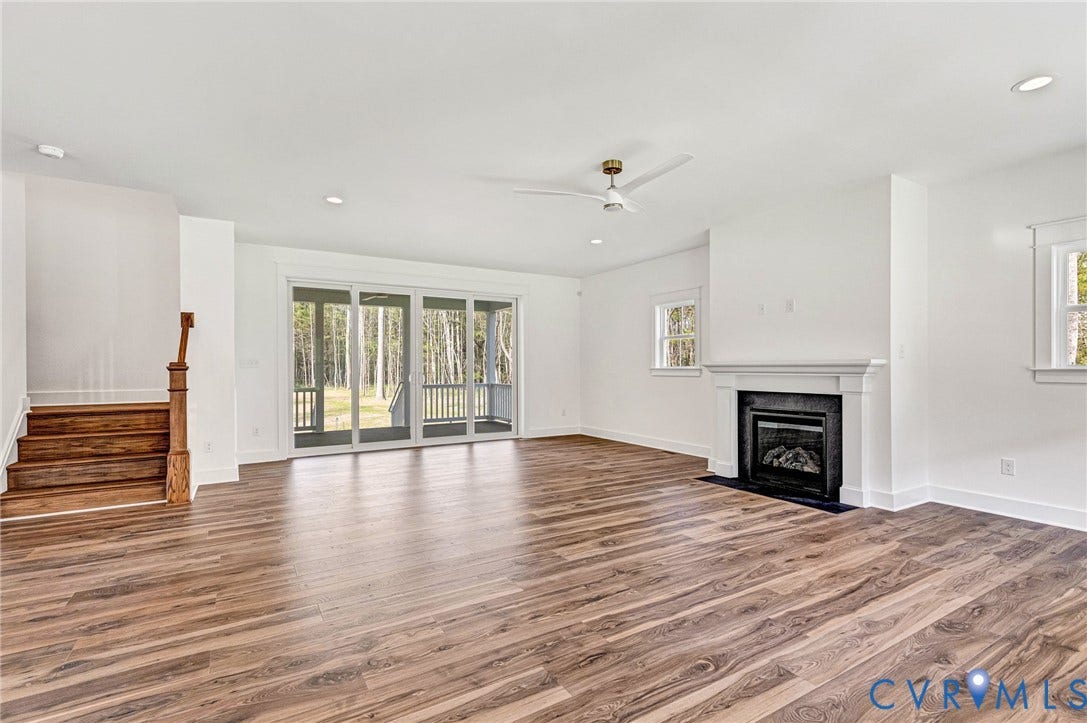 This spacious interior features wide plank flooring, a decorative fireplace with a classic white mantel, and a ceiling fan