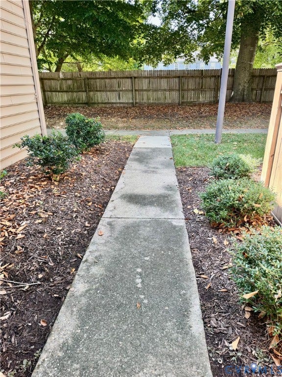 Concrete walkway flanked by planted shrubs and a wood fence