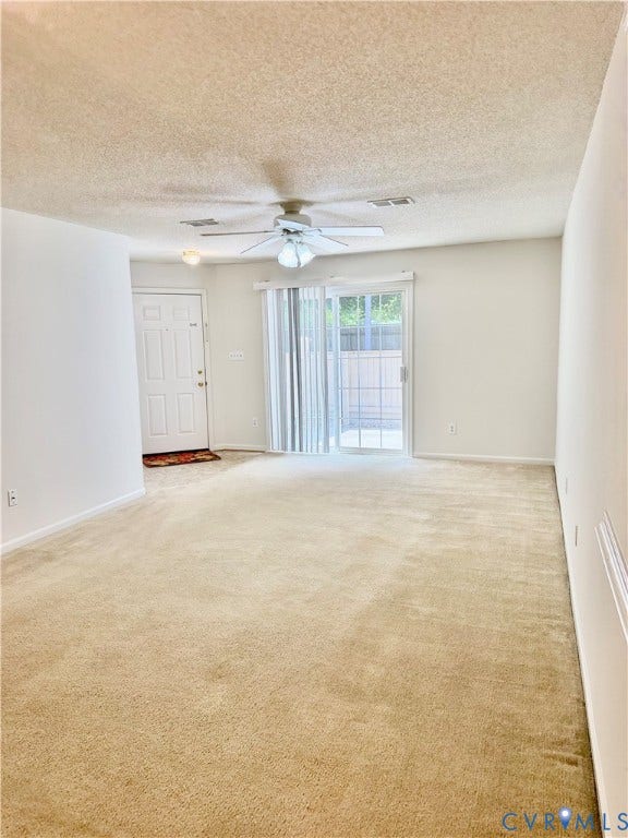 Expansive carpeted area with a ceiling fan, sliding glass door, and a paneled entry door