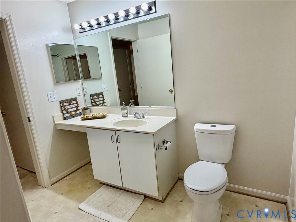 Vanity with integrated sink, a large wall-mounted mirror, and overhead strip lighting