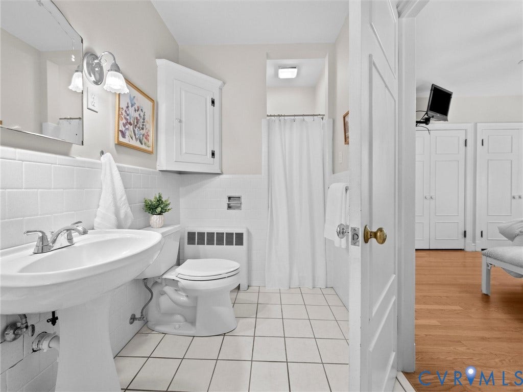216 Ross Road, Westham Area, Henrico, VA 23229 Pedestal sink with chrome fixtures, white subway tile wainscoting, white tile flooring, built-in wall cabinet, and a white shower curtain