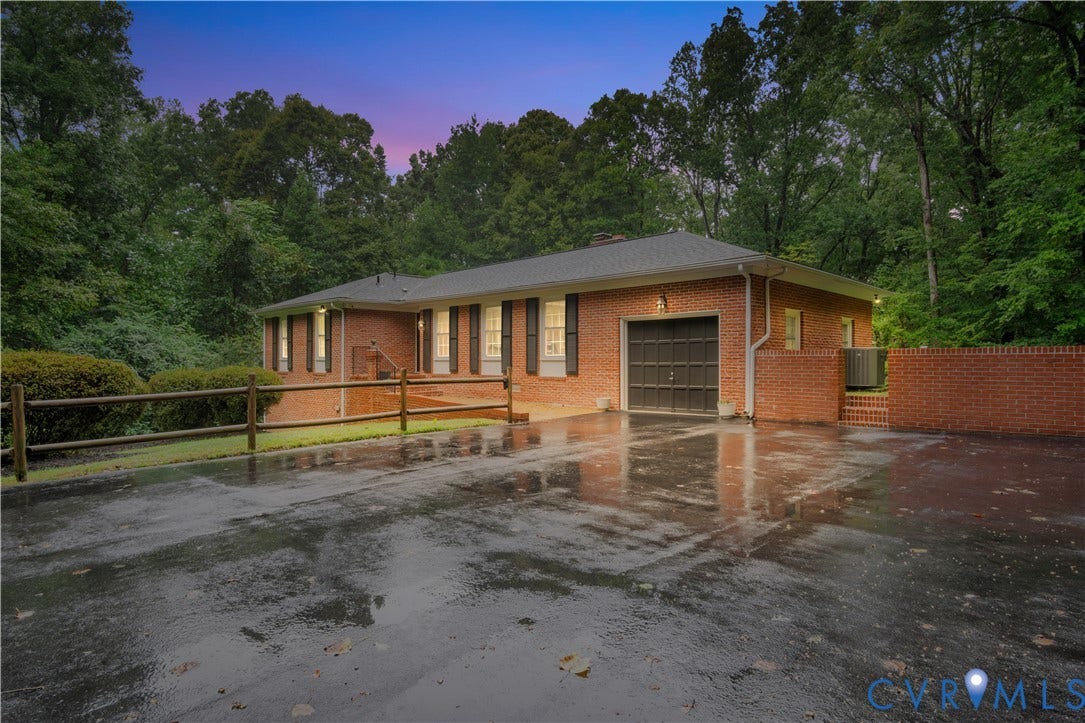 Brick exterior with dark shutters, attached garage, and a brick privacy wall