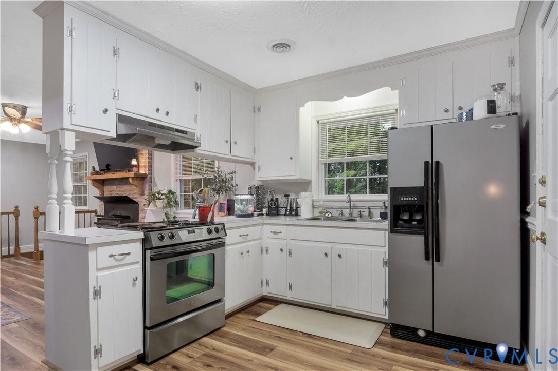 White cabinetry with integrated range hood, stainless steel appliances, wood-finish flooring, and a double basin sink