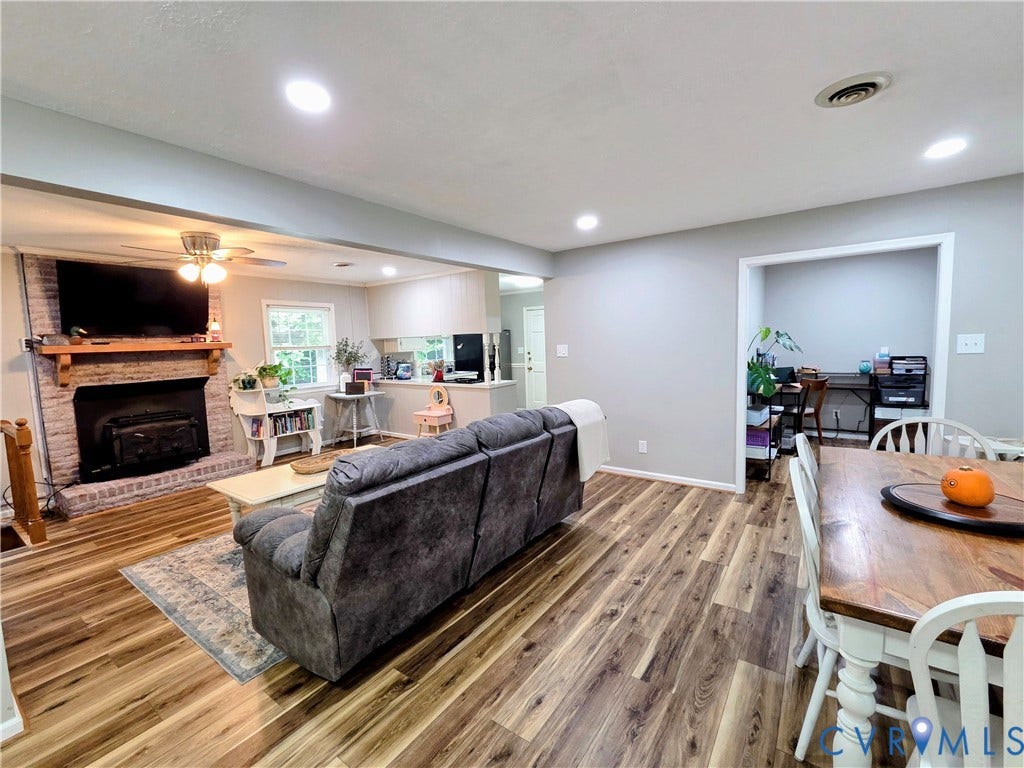 Open-concept living space featuring wood-finish flooring, a brick-surround fireplace with a wood mantel, recessed lighting, and a ceiling fan