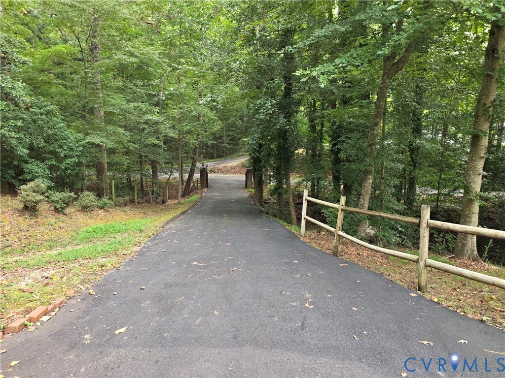 Asphalt driveway bordered by mature trees and a rustic wood fence