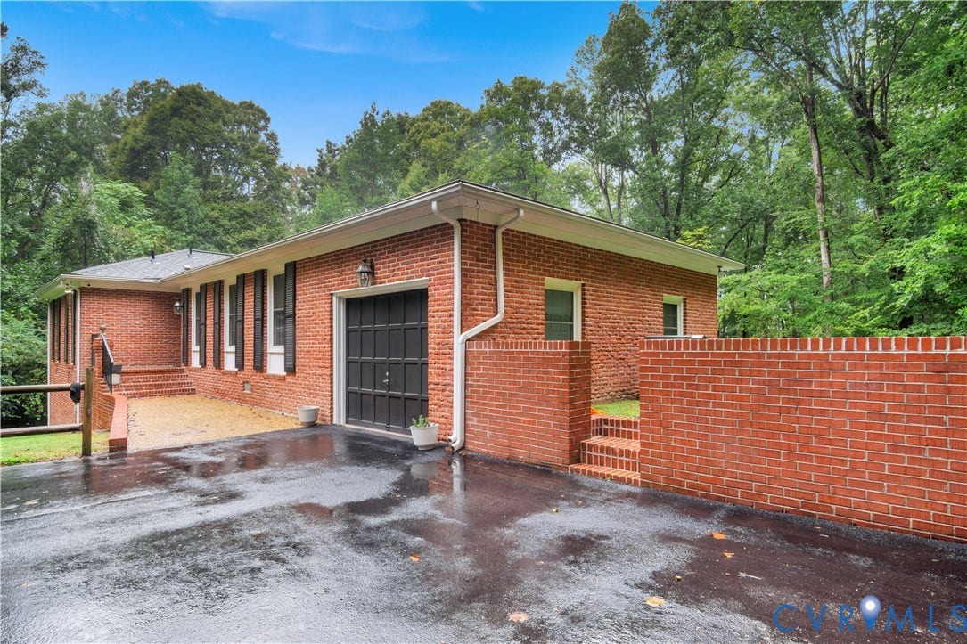 Brick exterior, black shutters, attached garage with panel door, brick retaining wall, and multiple steps