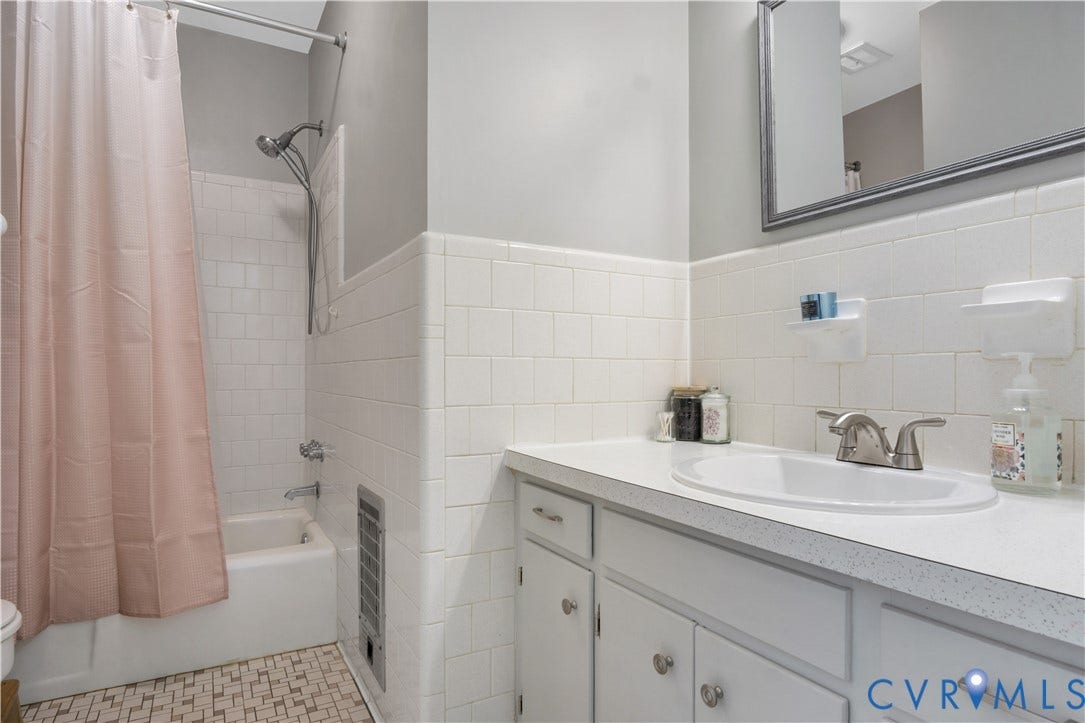 Bathroom featuring white subway tile surround, integrated bathtub with shower, vanity with an integrated sink, and a framed mirror