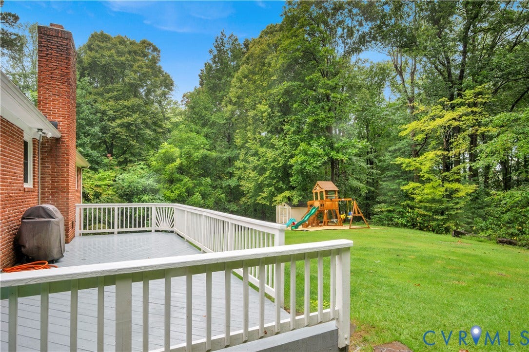 Expansive rear deck with white railing, brick exterior, and a lush green lawn surrounded by mature trees