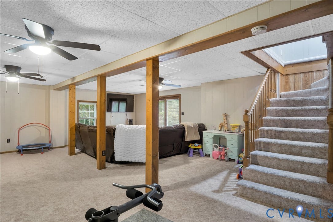 Carpeted lower level featuring exposed wood support beams and multiple ceiling fans