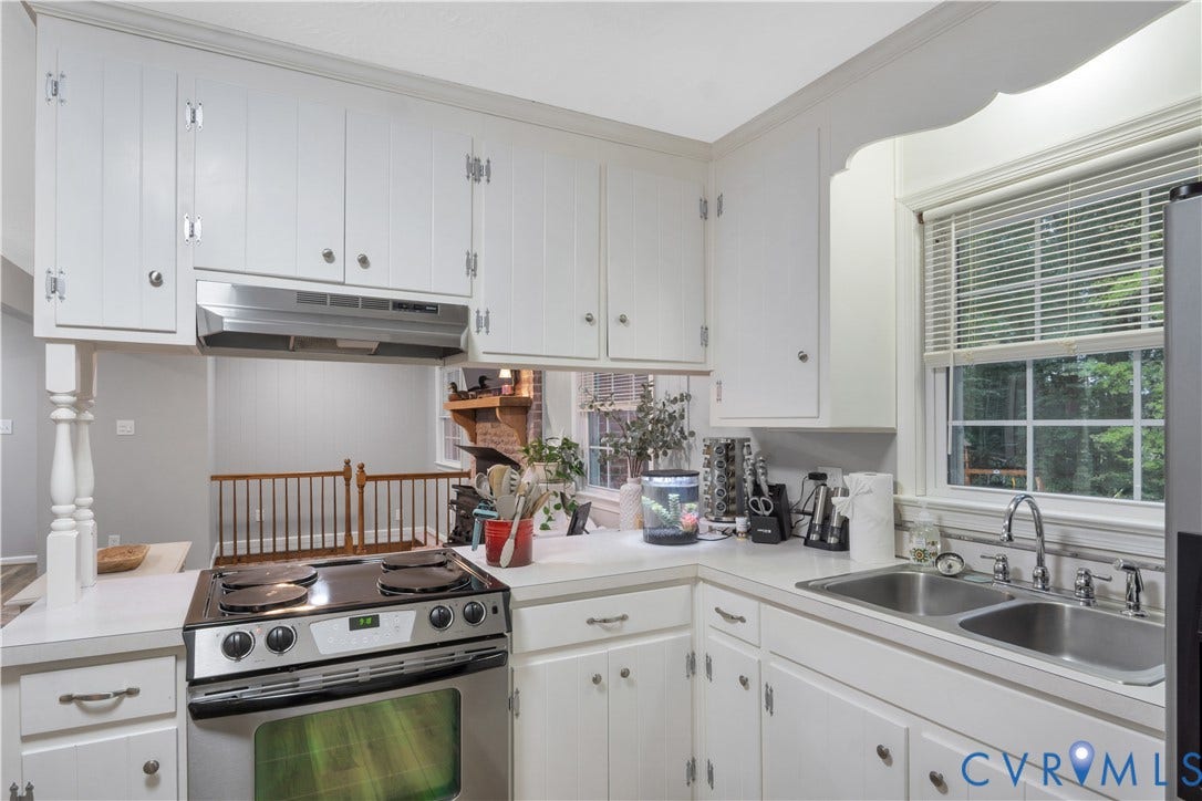 White cabinetry with silver hardware, dual basin stainless steel sink with a gooseneck faucet, window with blind, built-in range, and stainless steel range hood