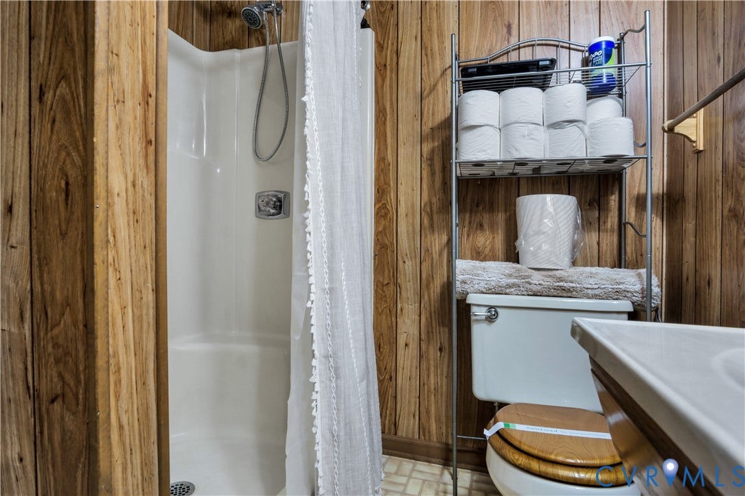 Wood-paneled bathroom with a white shower enclosure, chrome fixtures, and a white toilet