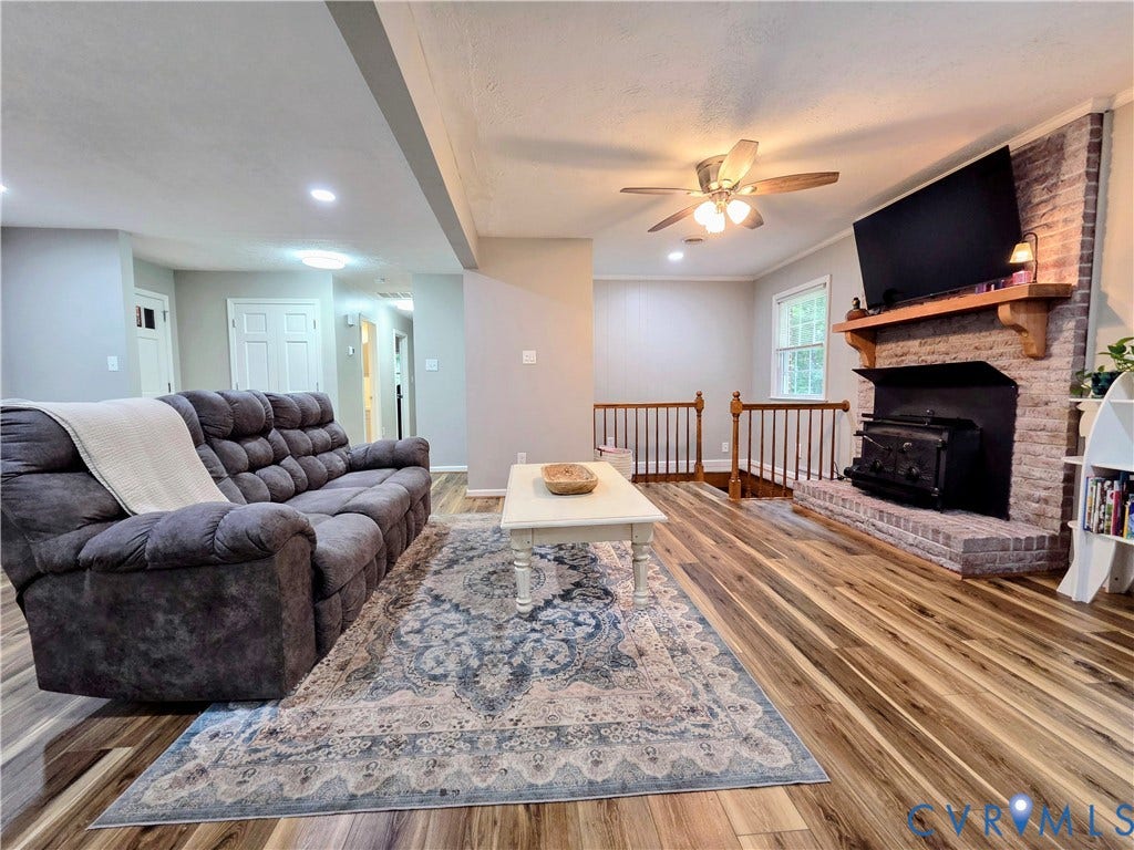 Brick fireplace with a wood-mantel, wood-finish flooring, and recessed ceiling lighting