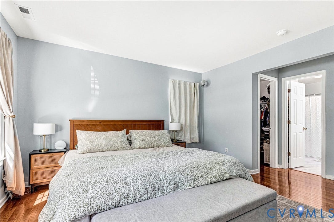 Hardwood flooring, wood-finish headboard, built-in closet with shelving, and window with drapes