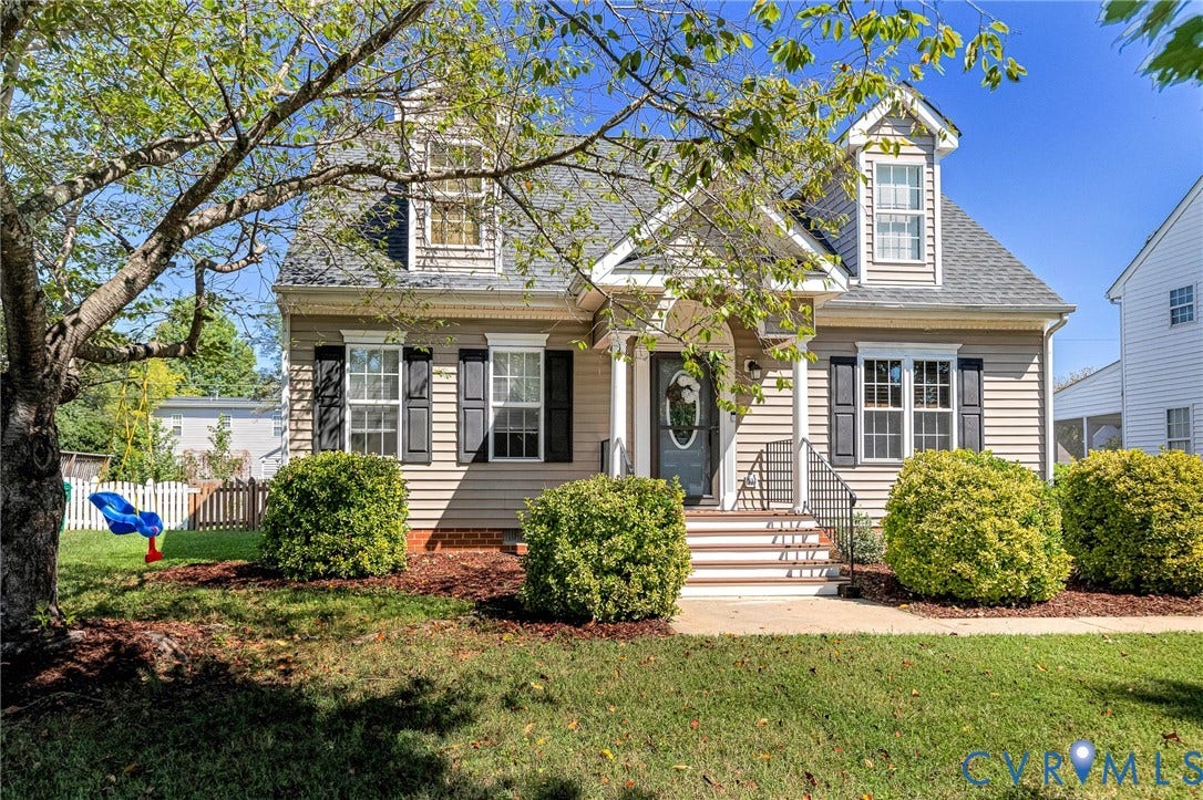 Front exterior featuring siding, dormer windows, a covered entry, and mature landscaping