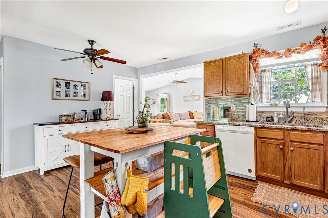 Kitchen with wood-finish flooring, a ceiling fan, wood cabinetry, a mosaic tile backsplash, and granite countertops