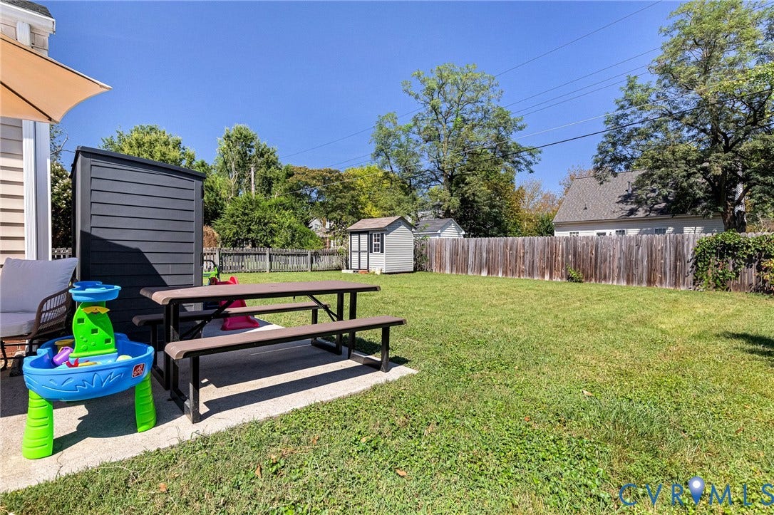 Expansive backyard featuring a manicured lawn, wood privacy fencing, and two storage sheds