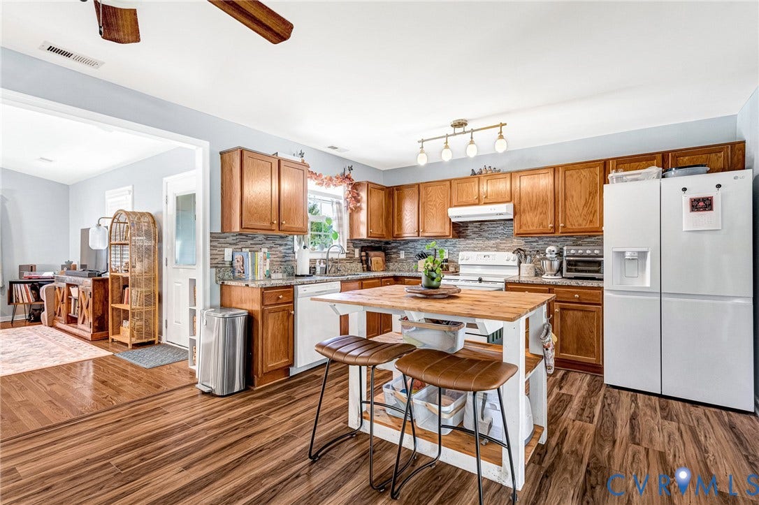 Wood-finish flooring throughout, wood cabinetry, stone countertops, tile backsplash, and a central island with a wood-finish top
