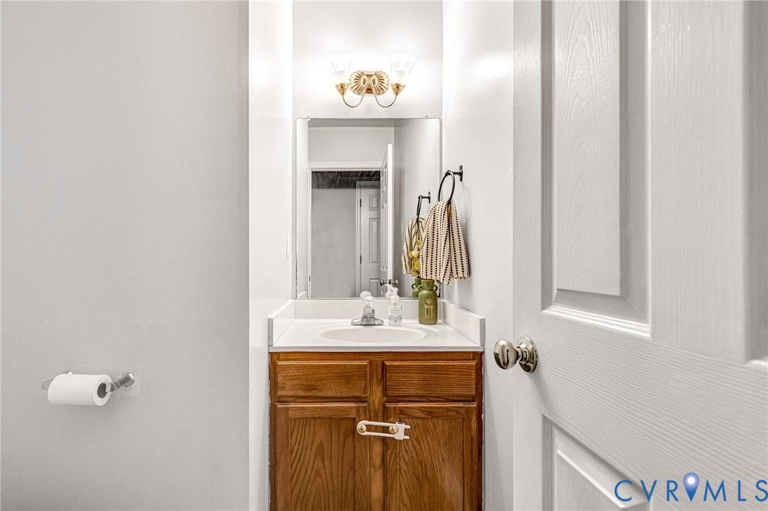 Wood-finish vanity with white countertop, undermount sink, and wall-mounted mirror