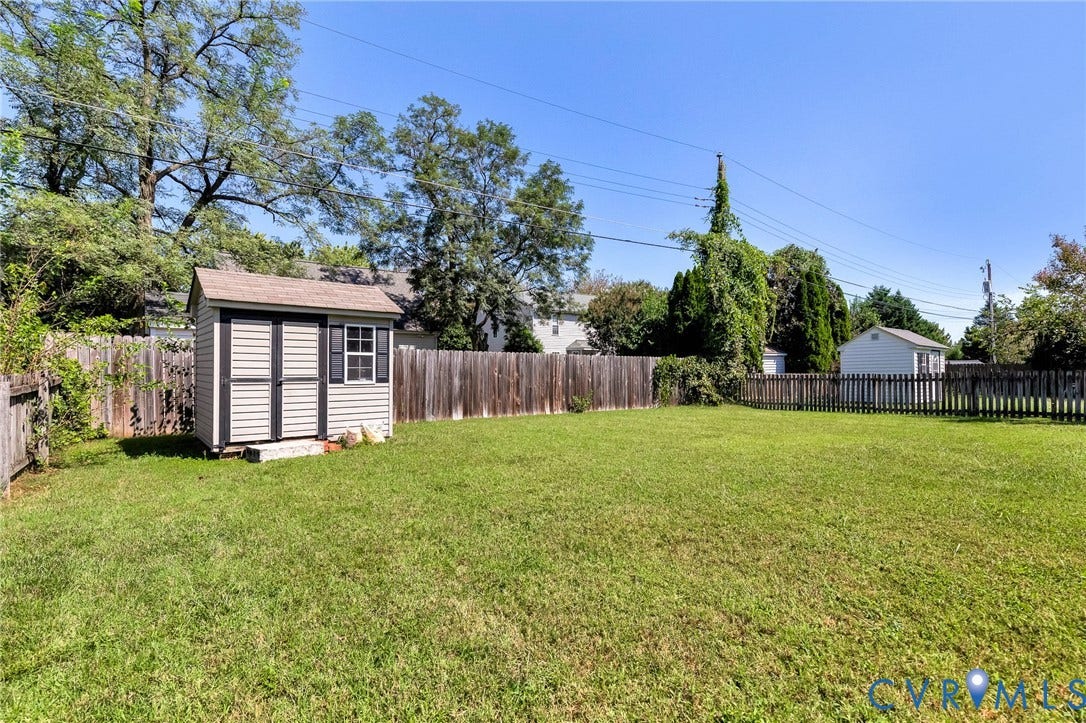Expansive green lawn featuring a storage shed with a window, a wooden privacy fence, and mature perimeter trees