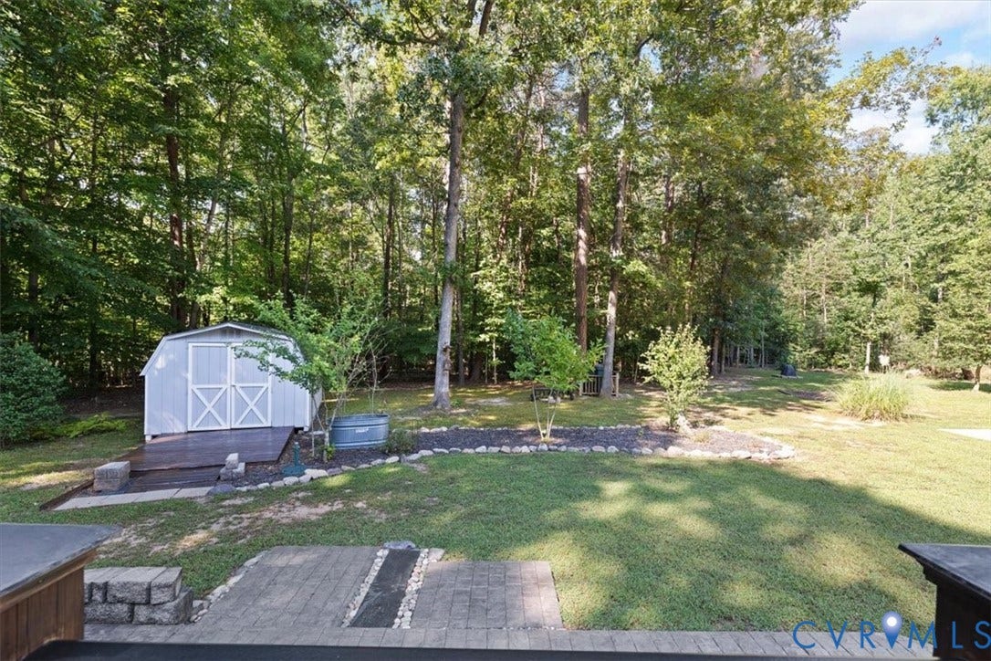 4398 Lynnecross Court, Powhatan, VA 23139 Detached storage shed with a wooden deck, surrounded by mature trees and a landscaped bed with decorative rocks
