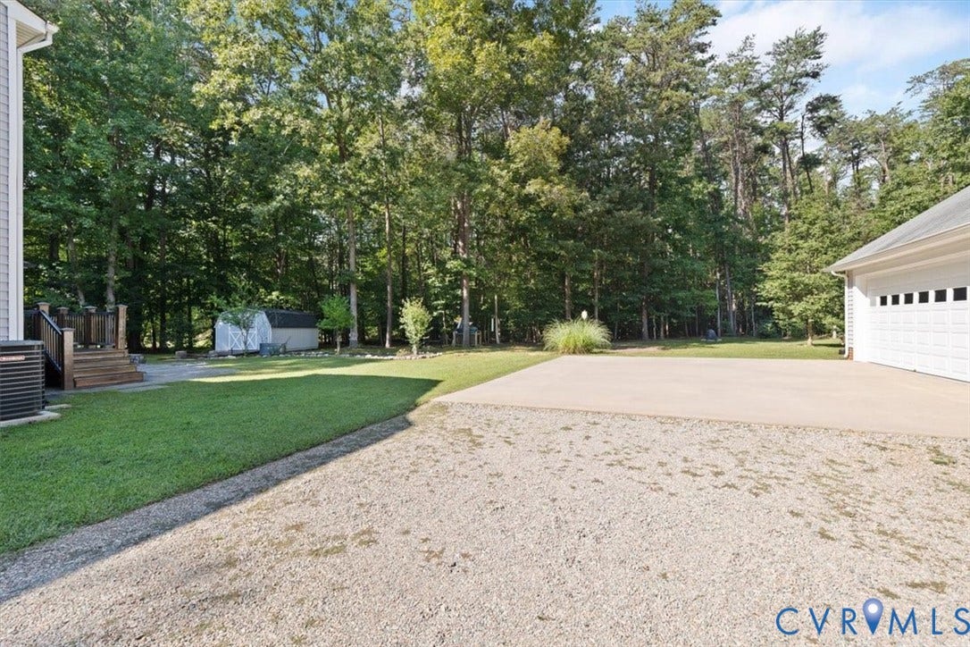 4398 Lynnecross Court, Powhatan, VA 23139 Expansive outdoor area featuring a detached garage with a white panel door, a concrete pad, a gravel drive, and a manicured lawn framed by mature trees