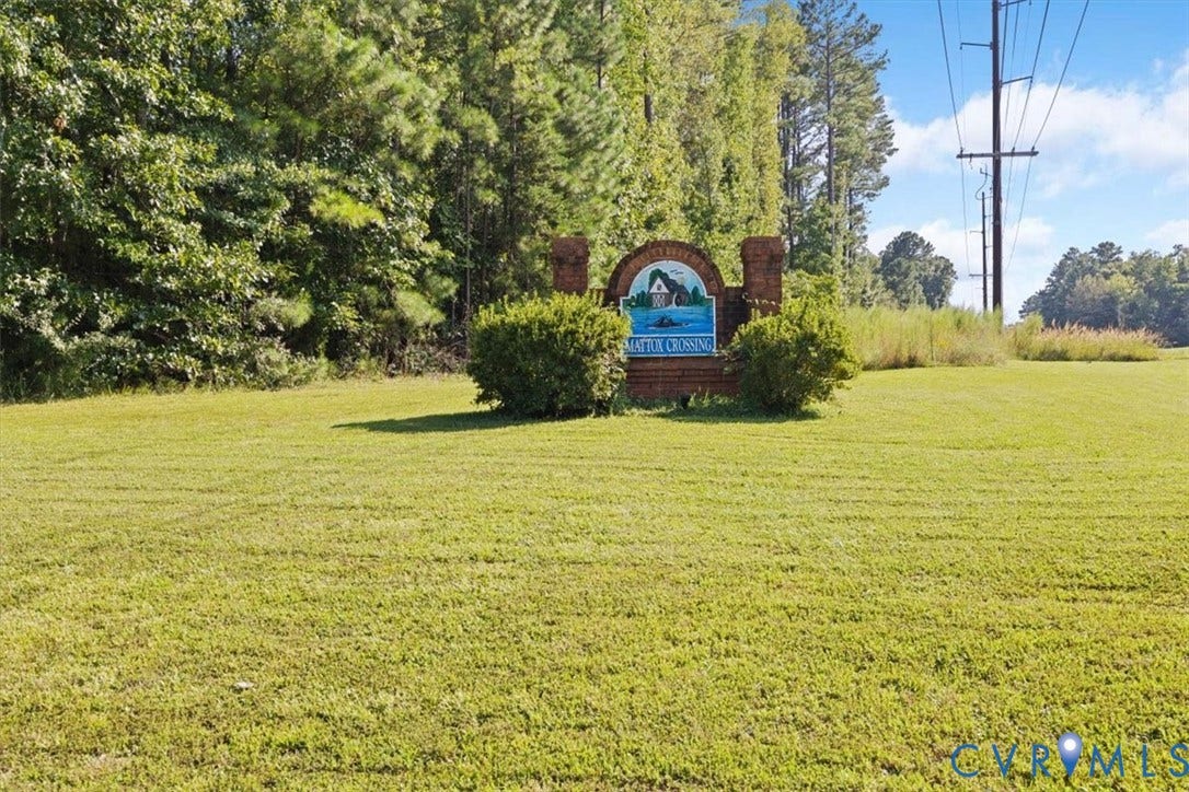4398 Lynnecross Court, Powhatan, VA 23139 Expansive grassy area with a brick sign structure featuring a decorative plaque, surrounded by established shrubbery and mature trees
