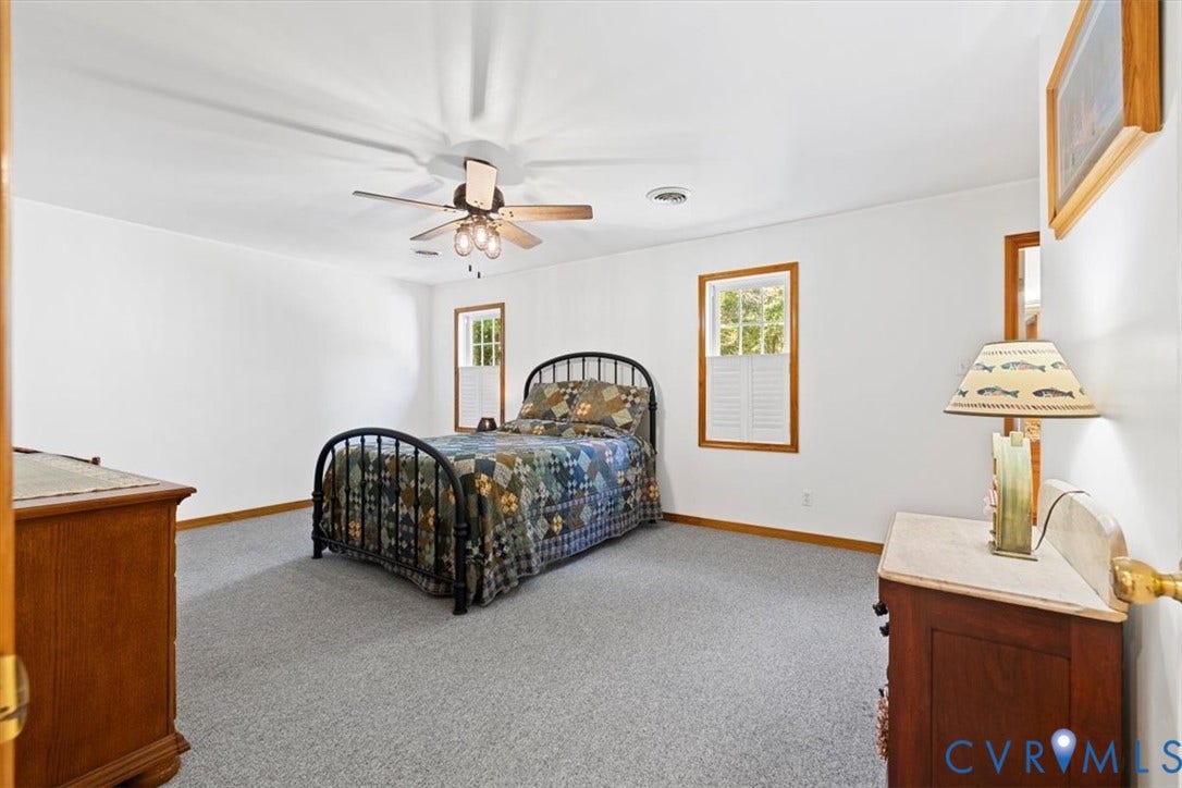 4398 Lynnecross Court, Powhatan, VA 23139 Neutral wall paint, ceiling fan with integrated lighting, two windows with wood trim, wood-finish baseboards, and grey carpeting