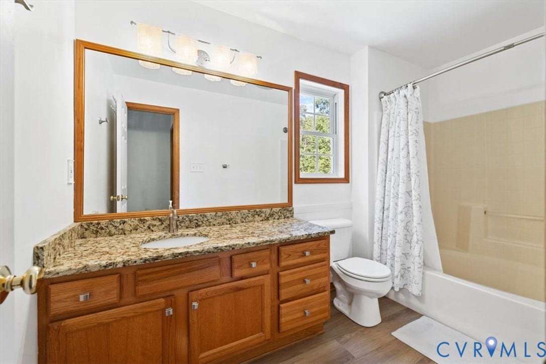 4398 Lynnecross Court, Powhatan, VA 23139 Wood-finish flooring, wood cabinetry with brushed nickel hardware, granite-style countertop with integrated sink, rectangular mirror with wood frame, and a window with wood trim