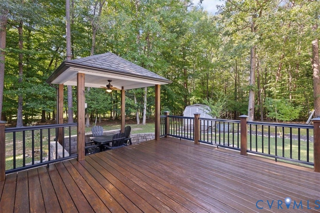 4398 Lynnecross Court, Powhatan, VA 23139 Expansive wood-finish deck with black metal railings, a covered gazebo featuring a ceiling fan, and a detached storage shed