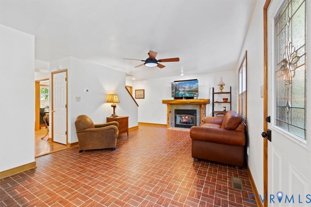 4398 Lynnecross Court, Powhatan, VA 23139 Living area featuring brick-pattern flooring, a ceiling fan, a fireplace with a stone surround and wood mantel, and a decorative front entry door