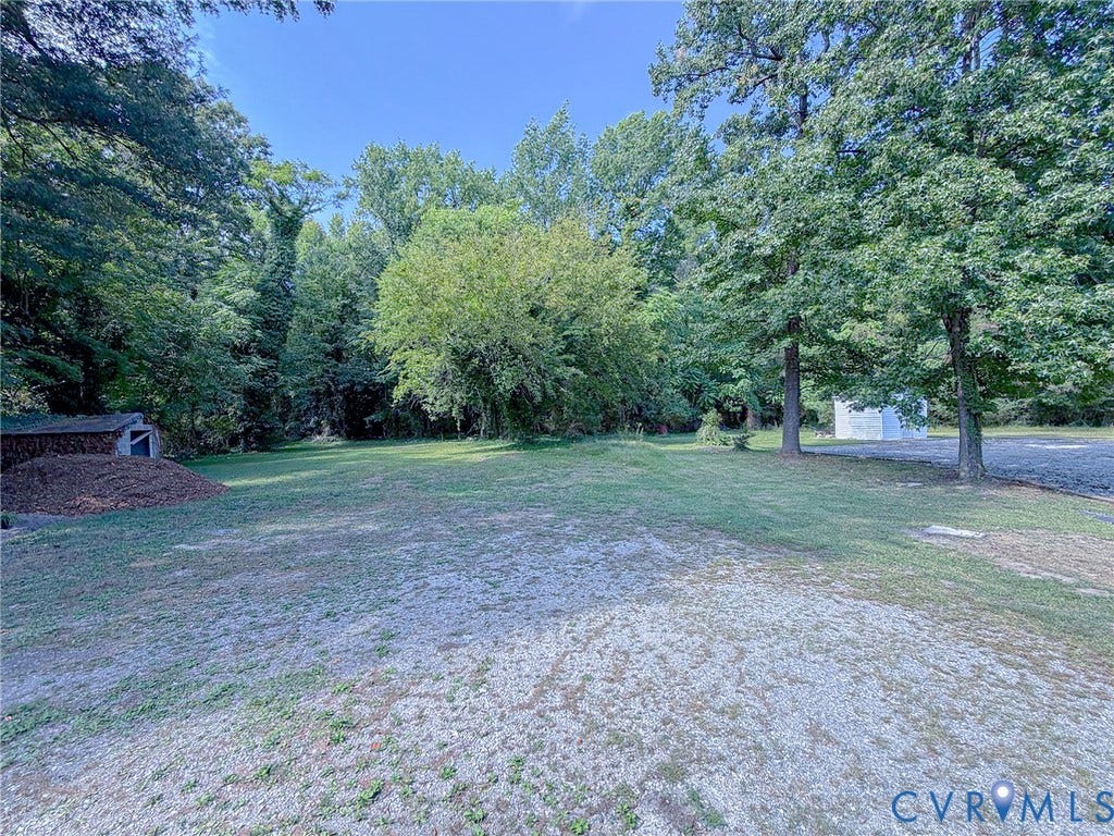 Expansive yard featuring a gravel area, a green lawn, and mature trees
