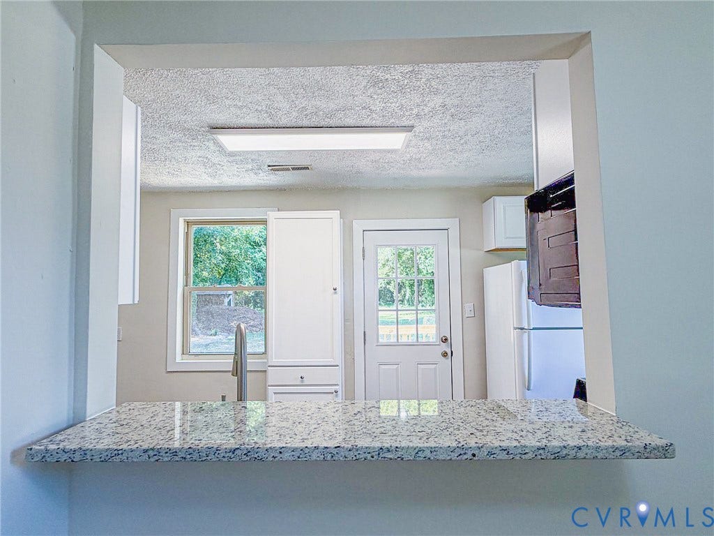 Pass-through window with a granite countertop, white cabinetry, and a stainless steel faucet
