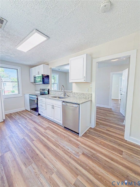 Kitchen featuring wood-finish flooring, white cabinetry, granite-style countertops, and stainless steel appliances