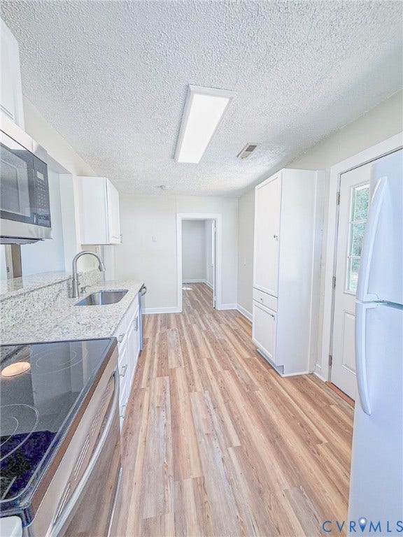 Kitchen featuring wood-finish flooring, white cabinetry, a stainless steel microwave, a stainless steel sink, and light-toned countertops